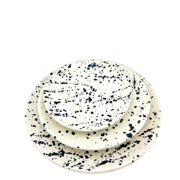 Set d’assiettes en céramique artisanale avec motif tacheté noir sur fond blanc cassé, empilées pour présentation.